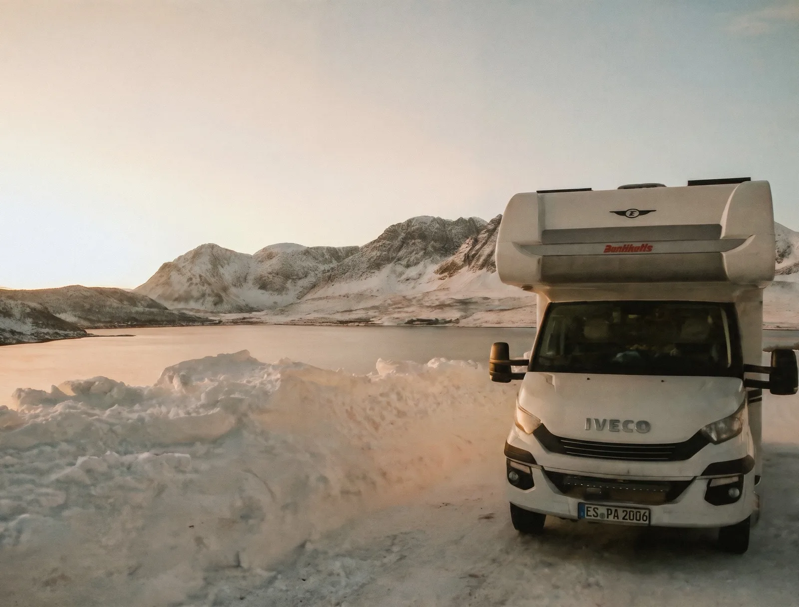 Ein Campingbus steht am Morgen an einem ruhigen Bergsee
